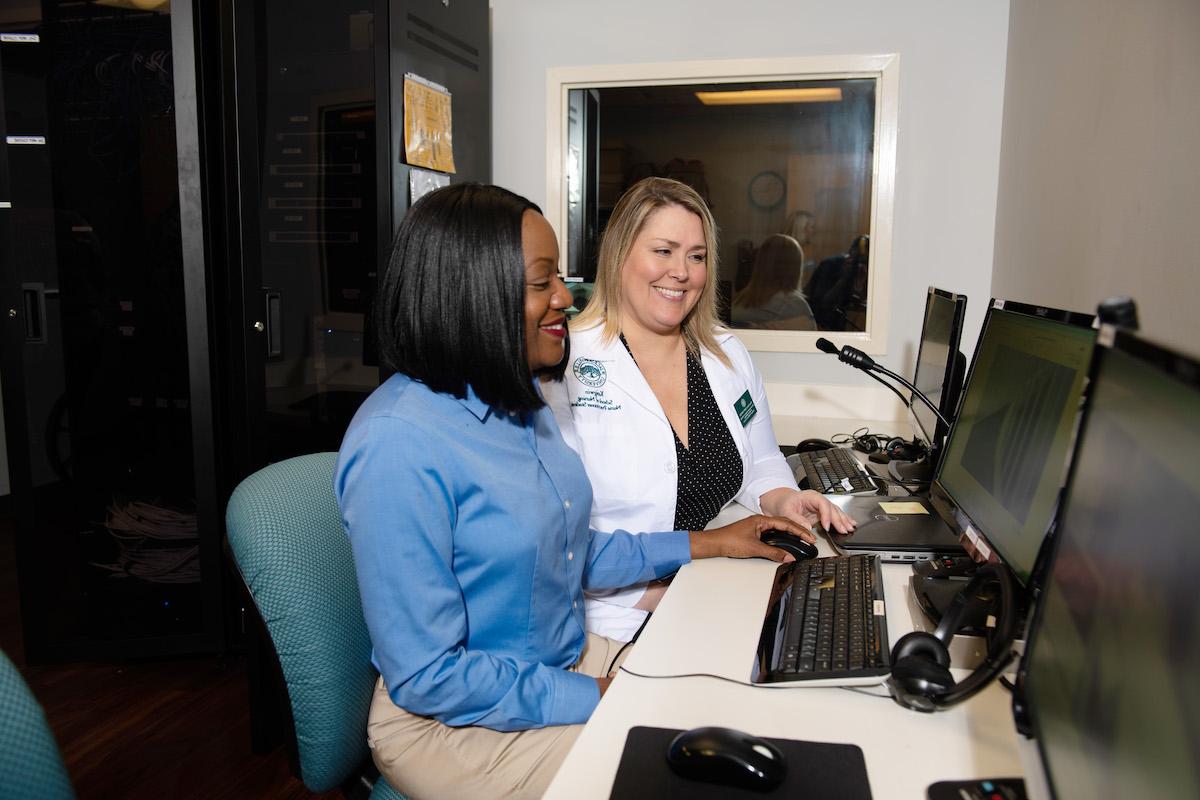 Female business student confers with a faculty member about information on a computer.